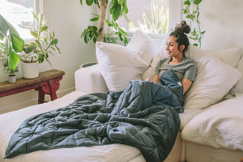 Model laying on white couch underneath the Nest Bedding Luxury Weighted Blanket