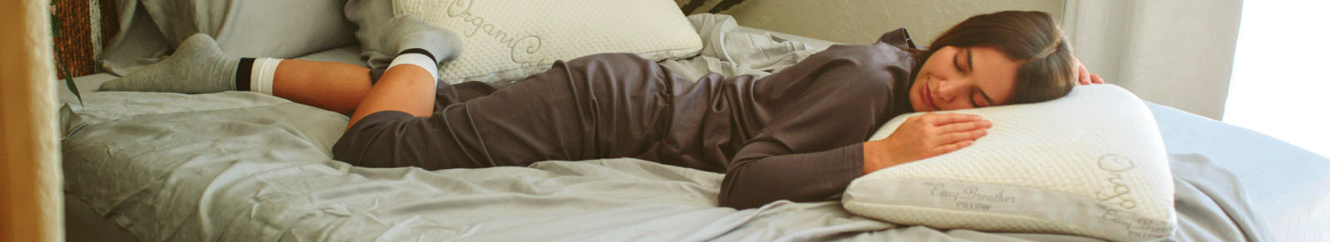 Woman laying on light gray bedding and resting her head on an easy breather natural latex pillow